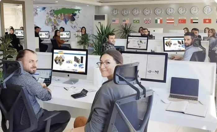 Open-plan sales office, staff at desks with APEX pages on screen